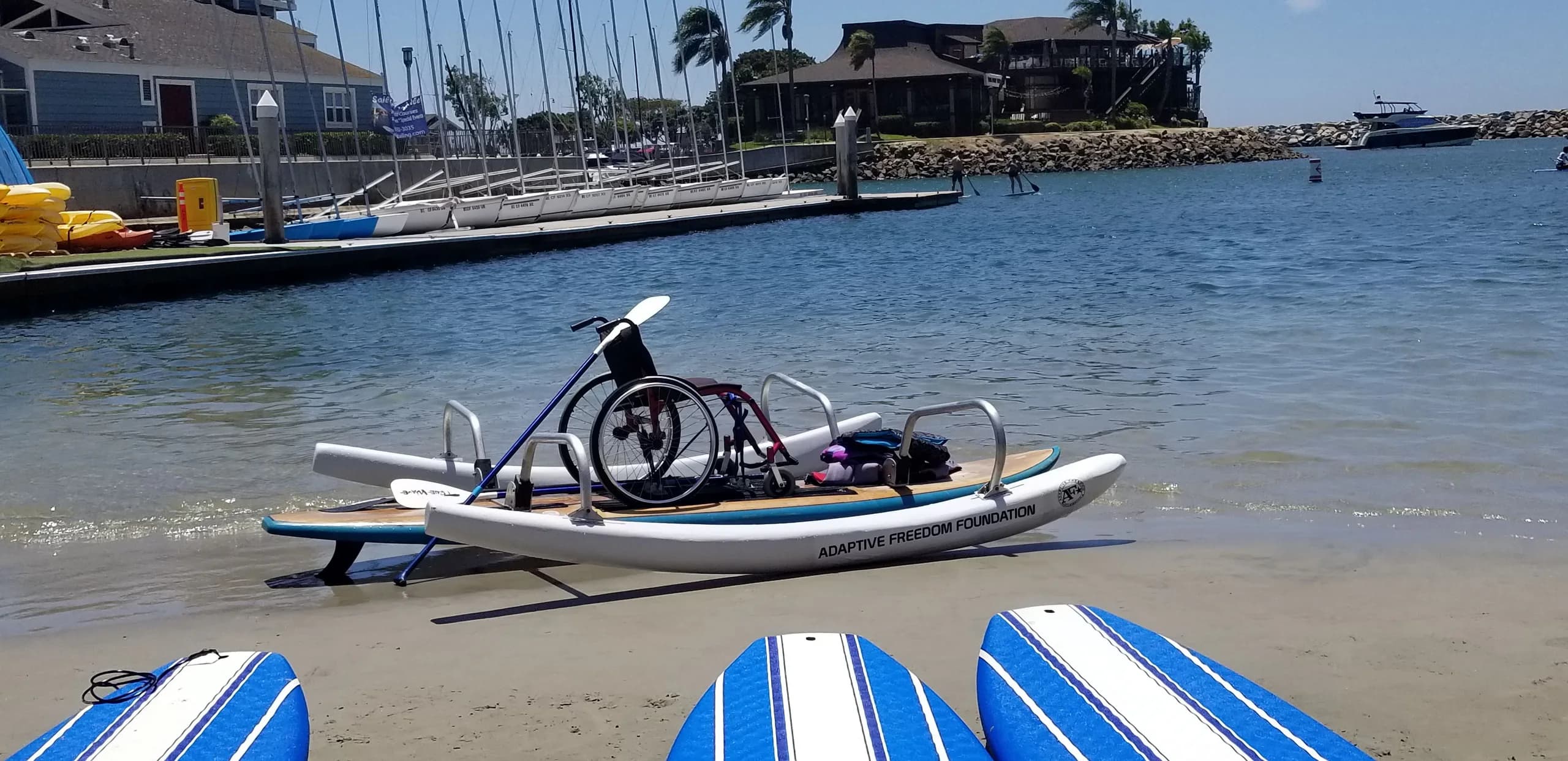 A wheelchair secured on an AFF adaptive paddleboard on the beach
