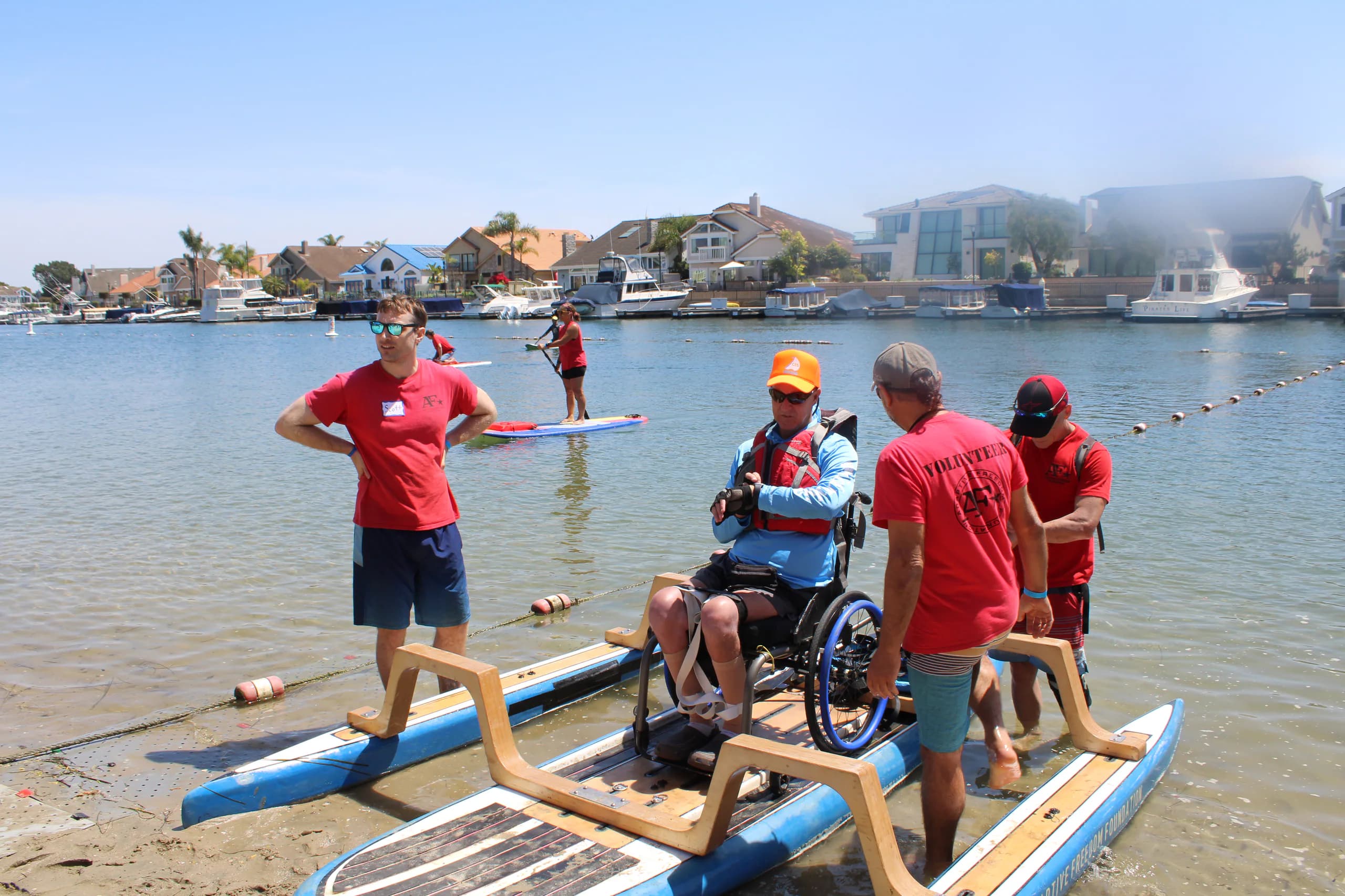 A wheelchair-adapted paddleboard and support crew preparing for a launch