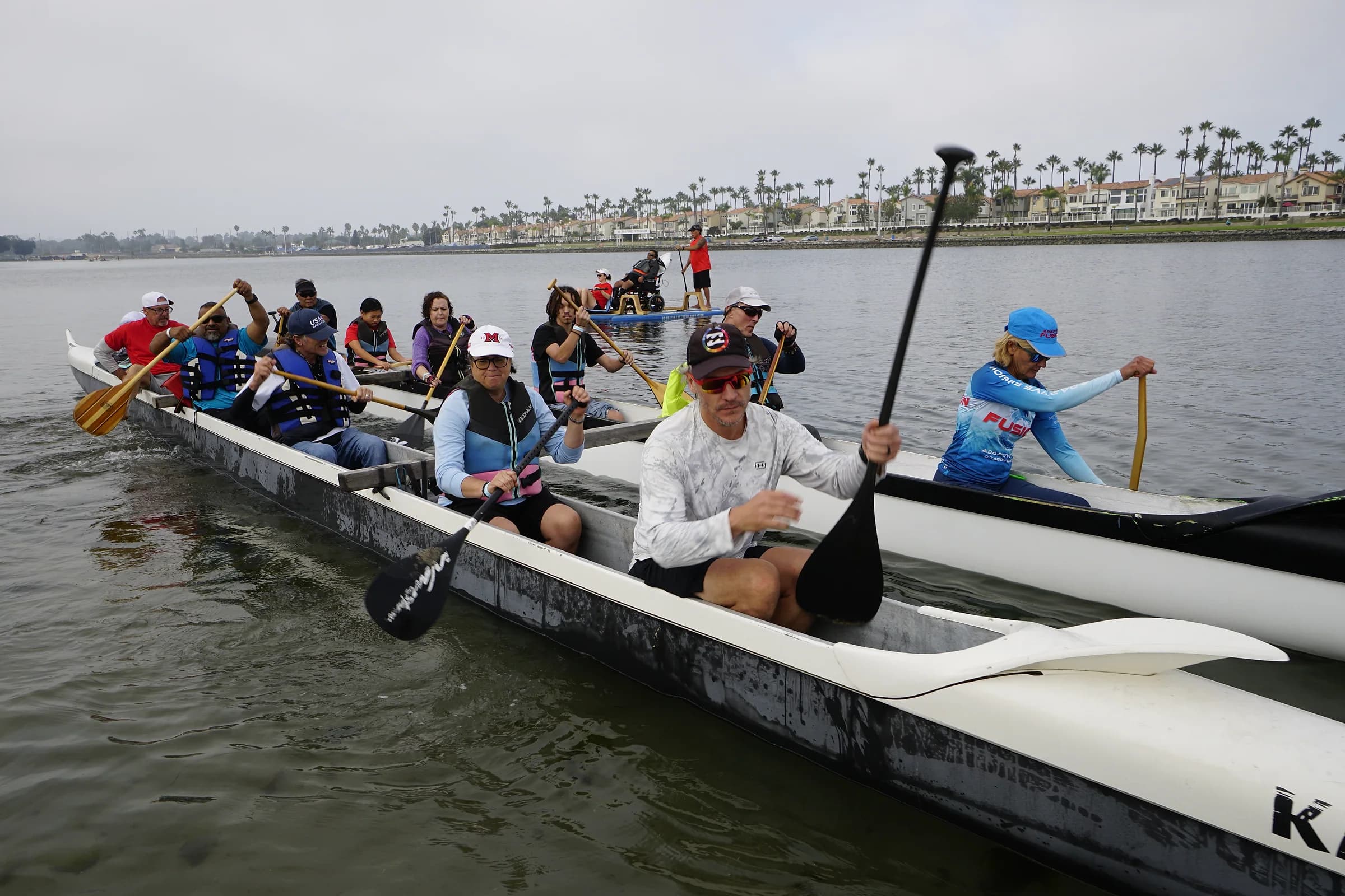 Adaptive paddlers and volunteers moving together in a long outrigger canoe