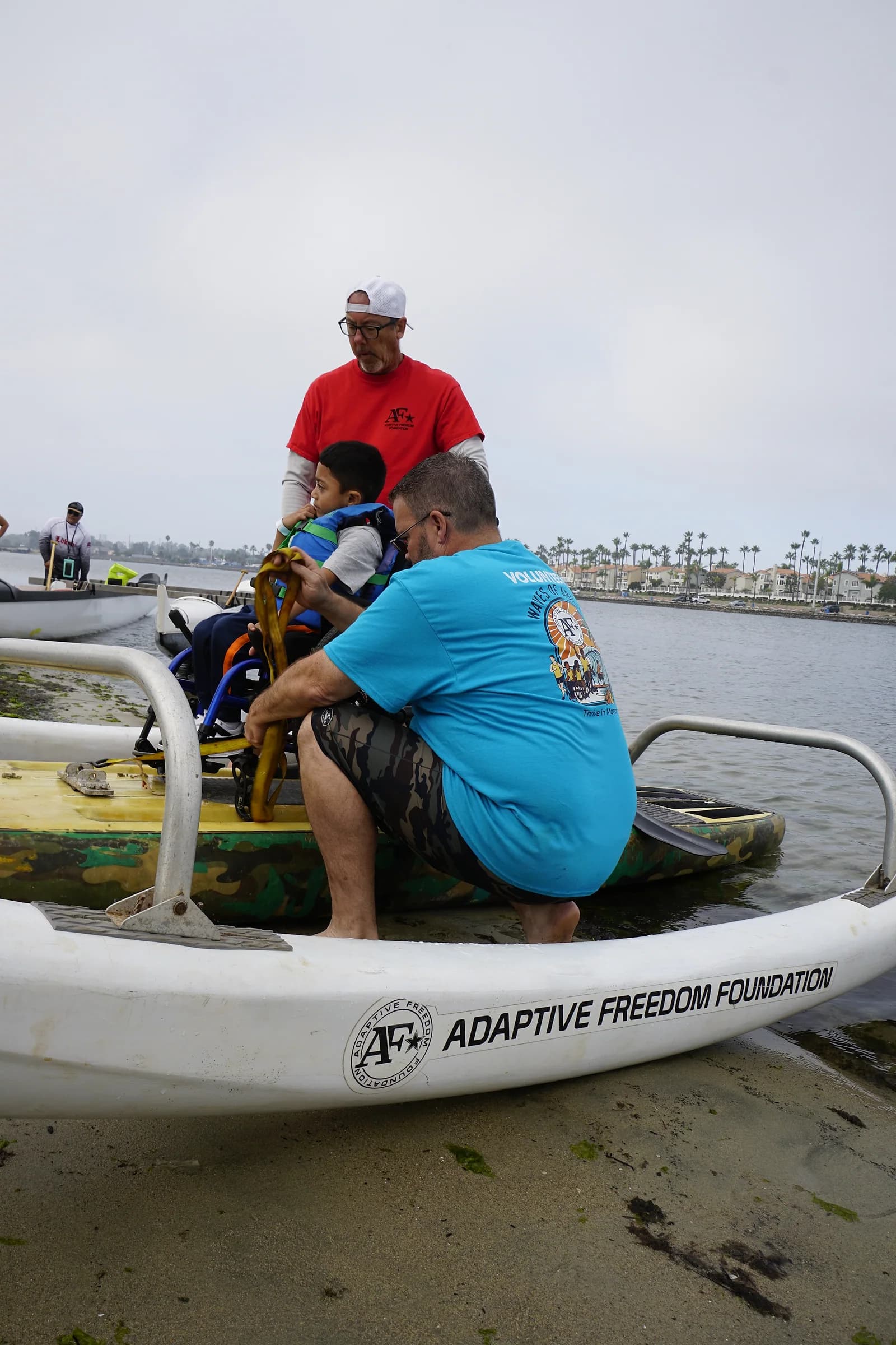 Two volunteers carefully assisting a wheelchair user onto an adaptive board