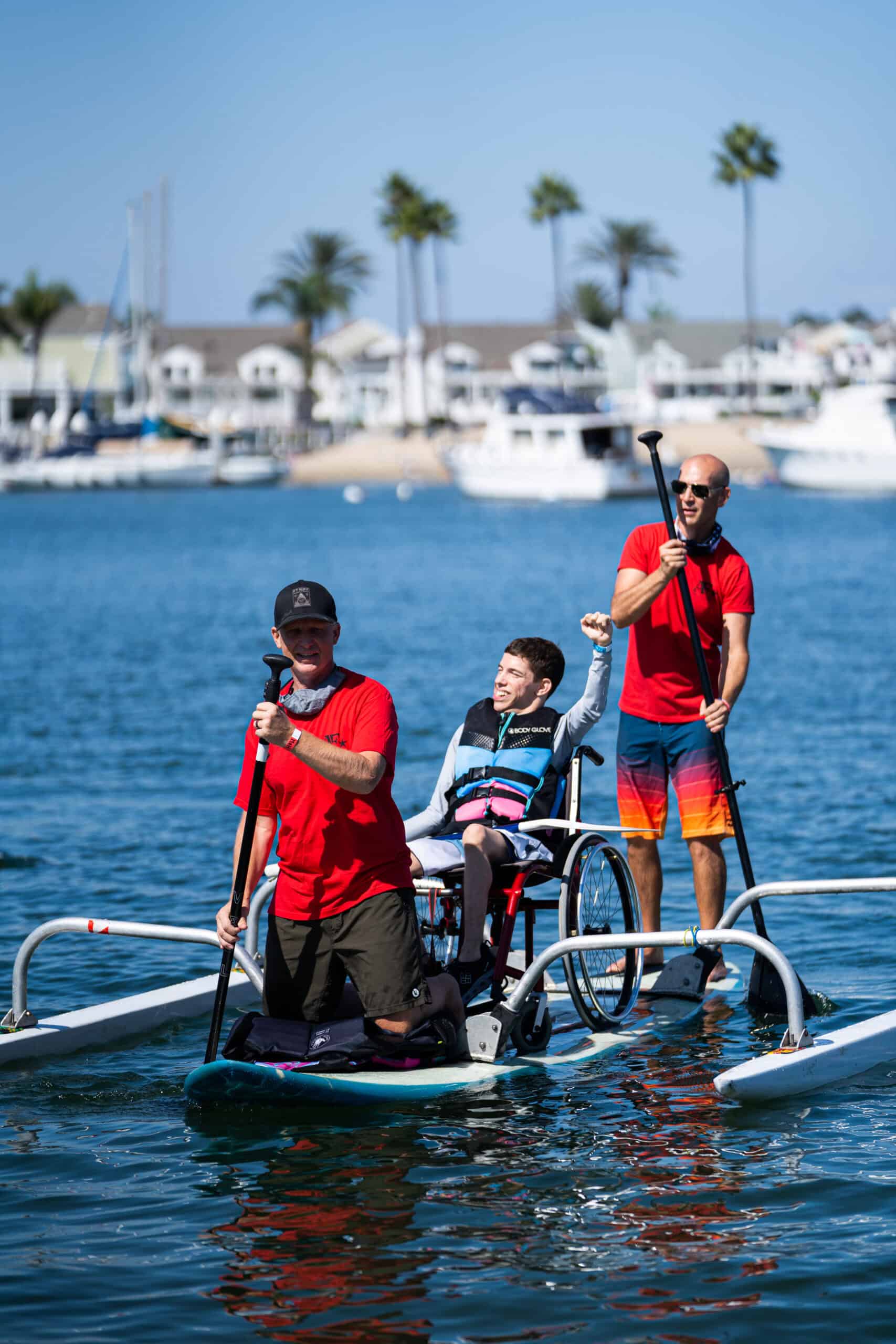 Excited young man in wheelchair on an adaptive paddle board raising his arm in the air